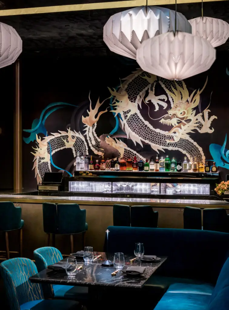 Gekko’s green room bar with teal seating, a backlit liquor display, and a bold dragon mural as the backdrop.