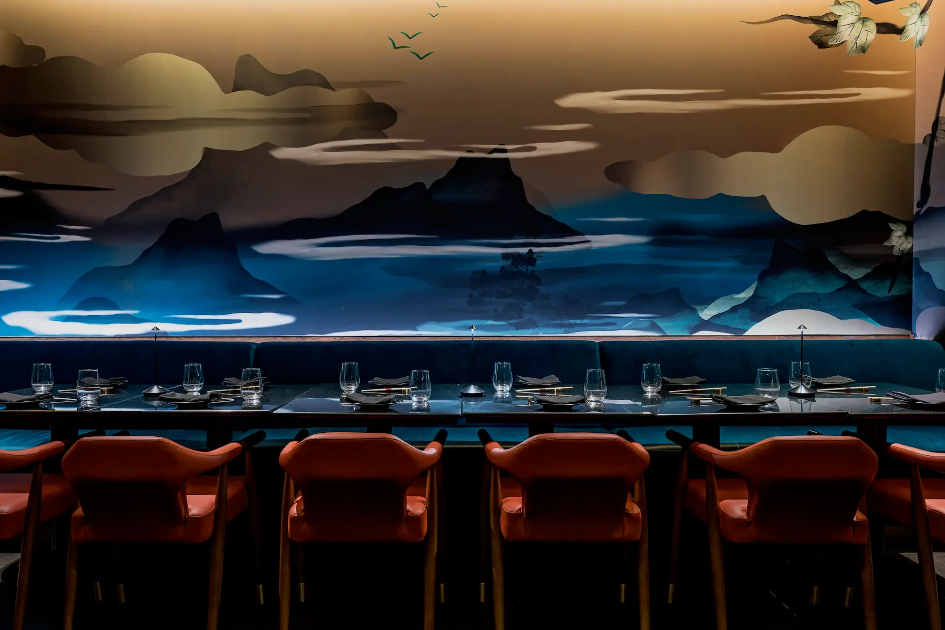 Elegant private dining room at Gekko, featuring a moody landscape mural, teal banquette seating, coral chairs, and a sleek table set with modern glassware and chopsticks.